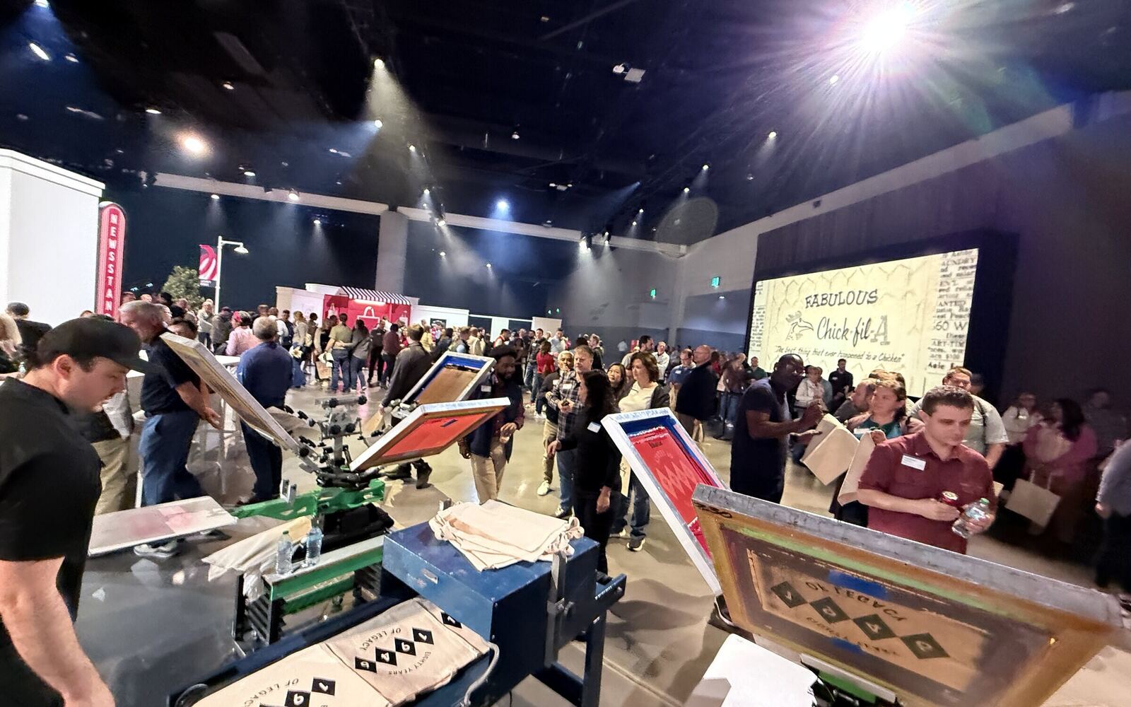 Wide view of a large indoor event floor with a manual print station running in the foreground and a full crowd of guests behind it