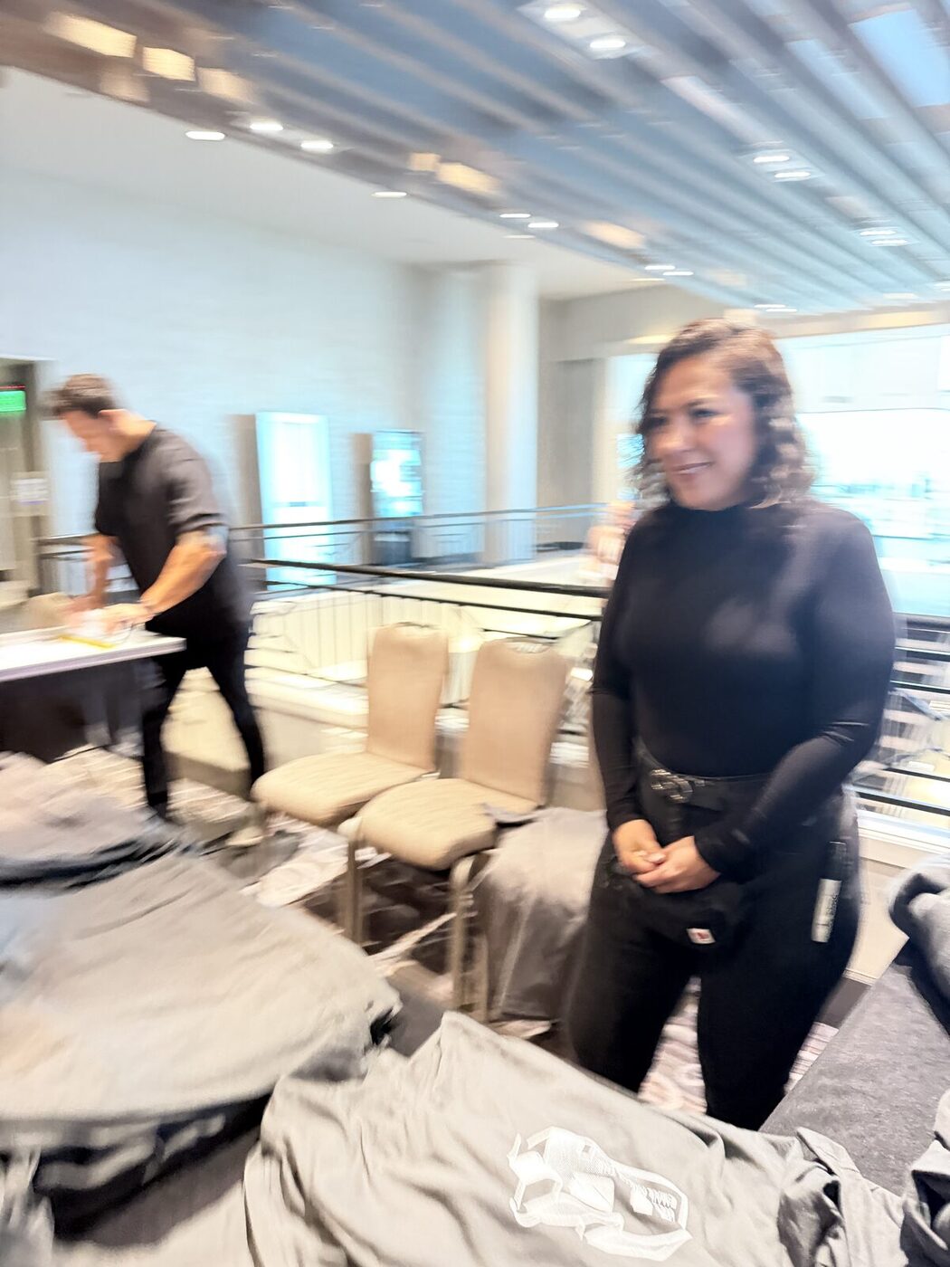 Two crew members folding and staging freshly printed shirts on tables inside a corporate venue