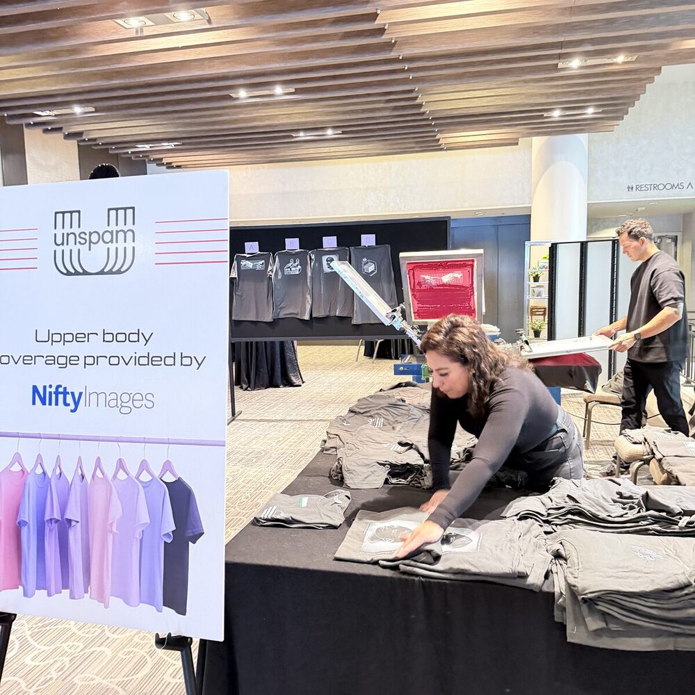 Crew member squaring up freshly printed shirts on a staging table beside a conference signage board